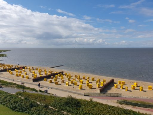 Strand mit gelben Strandkörben und ruhigem Wasser unter wolkigem Himmel.